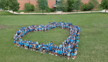 Kids stand in the shape of a heart in a field
