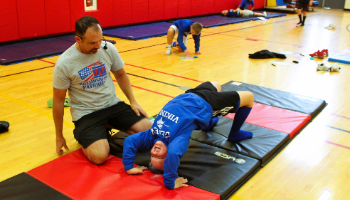 Mr Graham helps a student in a bridge position on a colorful mat