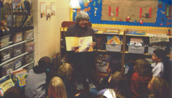 A person reads a book to a class of students 